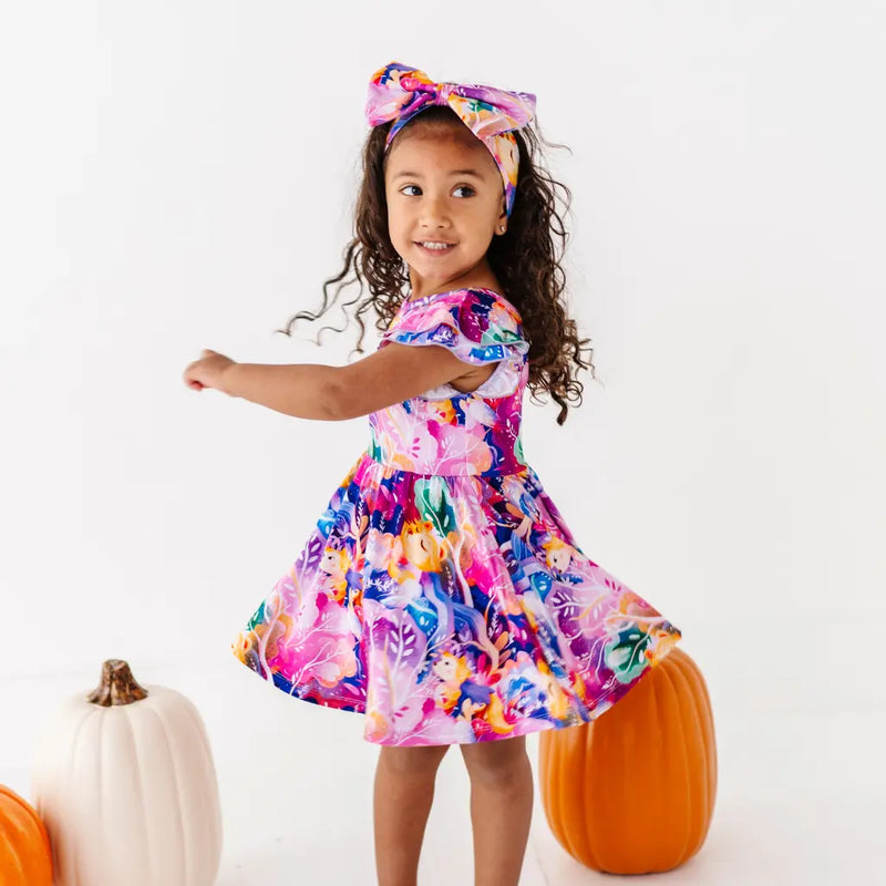 Young girl in a colorful floral dress with pumpkins on a white background