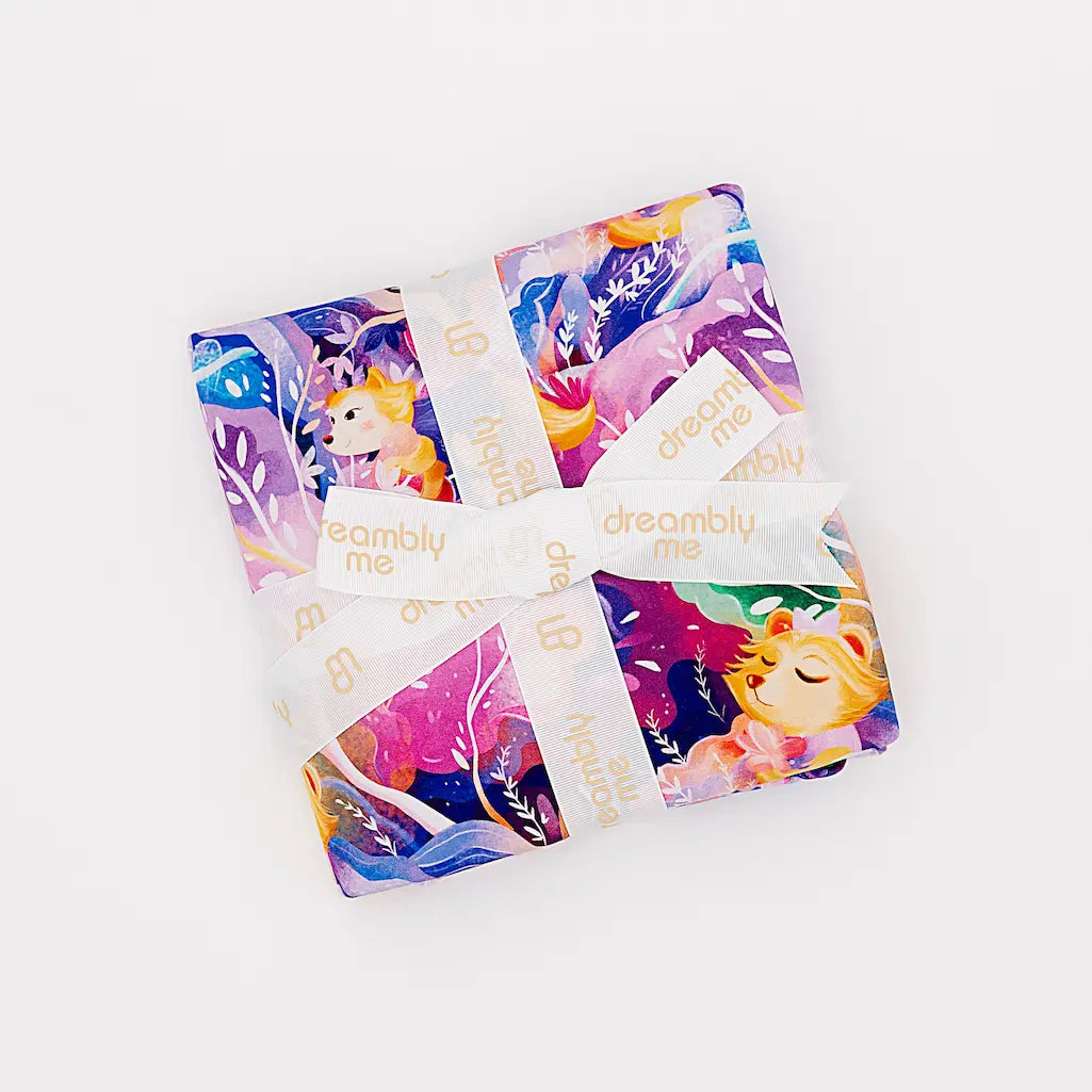 Colorful Dreambly Me packaging featuring vibrant cartoon characters and branding, tied with a cream ribbon, displayed on a white background