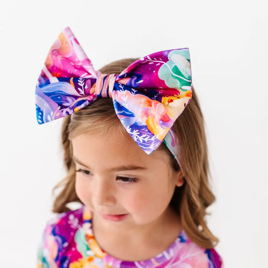 Child wearing a colorful floral headband with a large bow on a white background