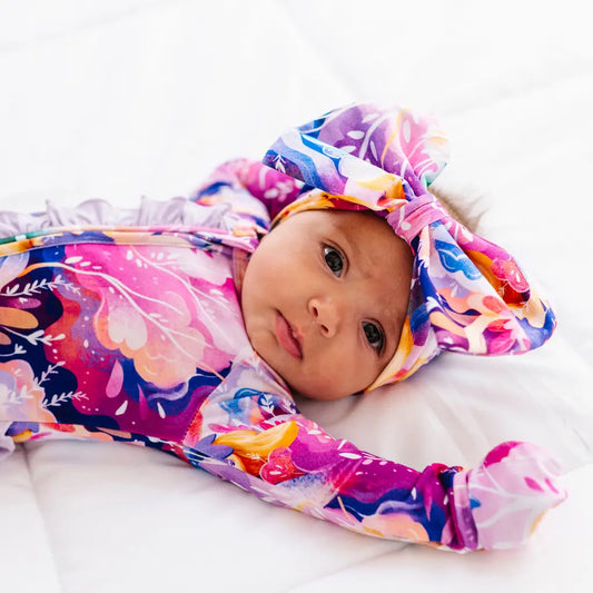 Baby wrapped in a colorful floral swaddle with a matching headband on a white background