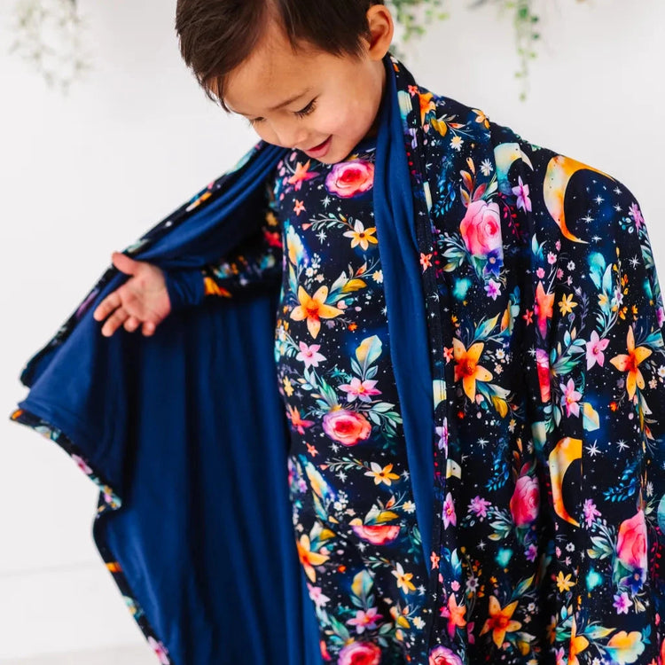 Child wearing a colorful floral and night sky patterned outfit with a blue shawl.