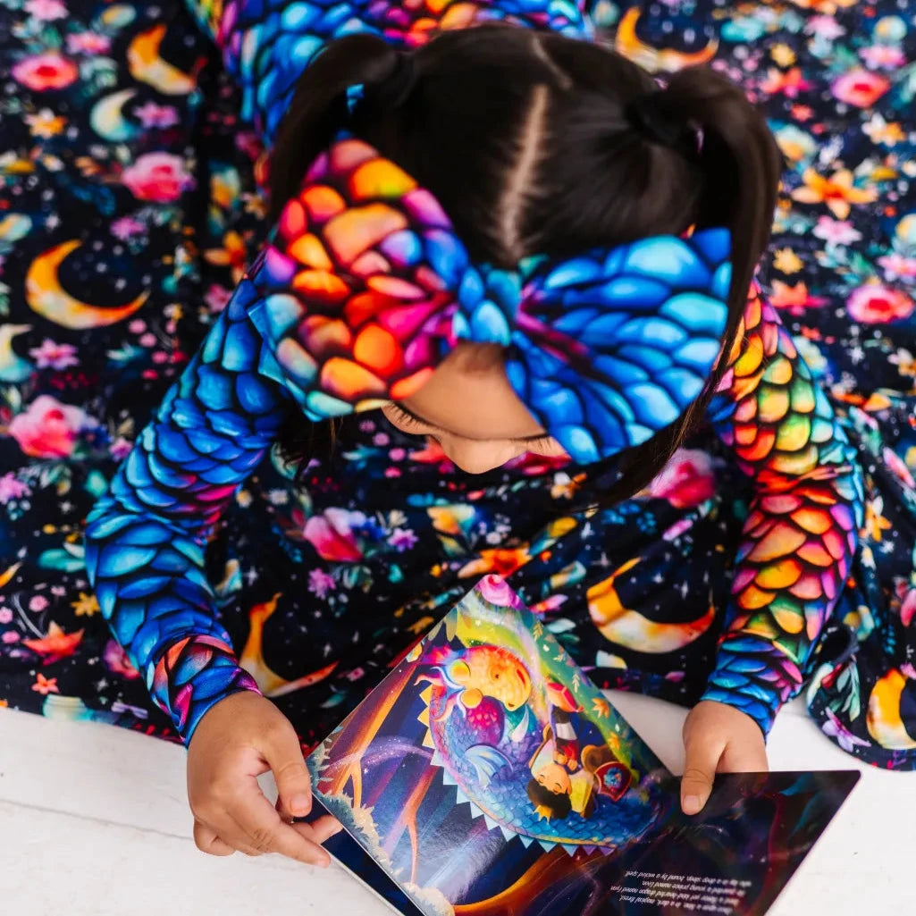A child wearing a colorful bow headband with a dragon scale pattern in rainbow colors, reading a book.
