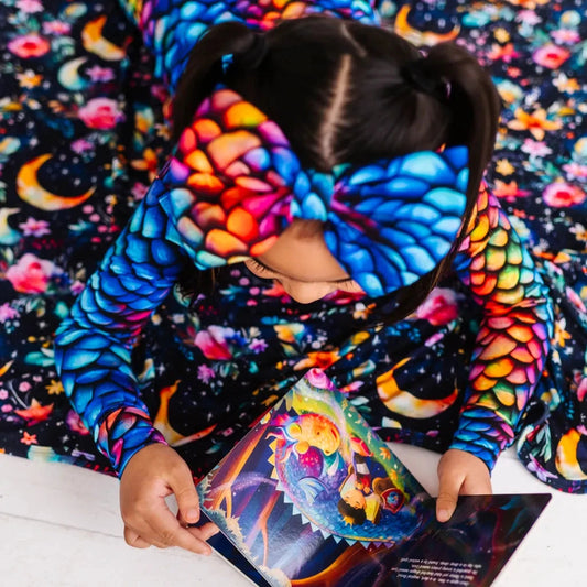 A child wearing a colorful bow headband with a dragon scale pattern in rainbow colors, reading a book.