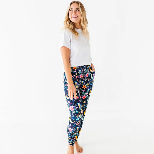 A woman standing and smiling, wearing white shirt and multicolored floral pajama pants with tapered ankles and side pockets.