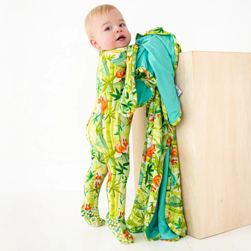 Baby in a colorful onesie standing next to a mattress on a white background