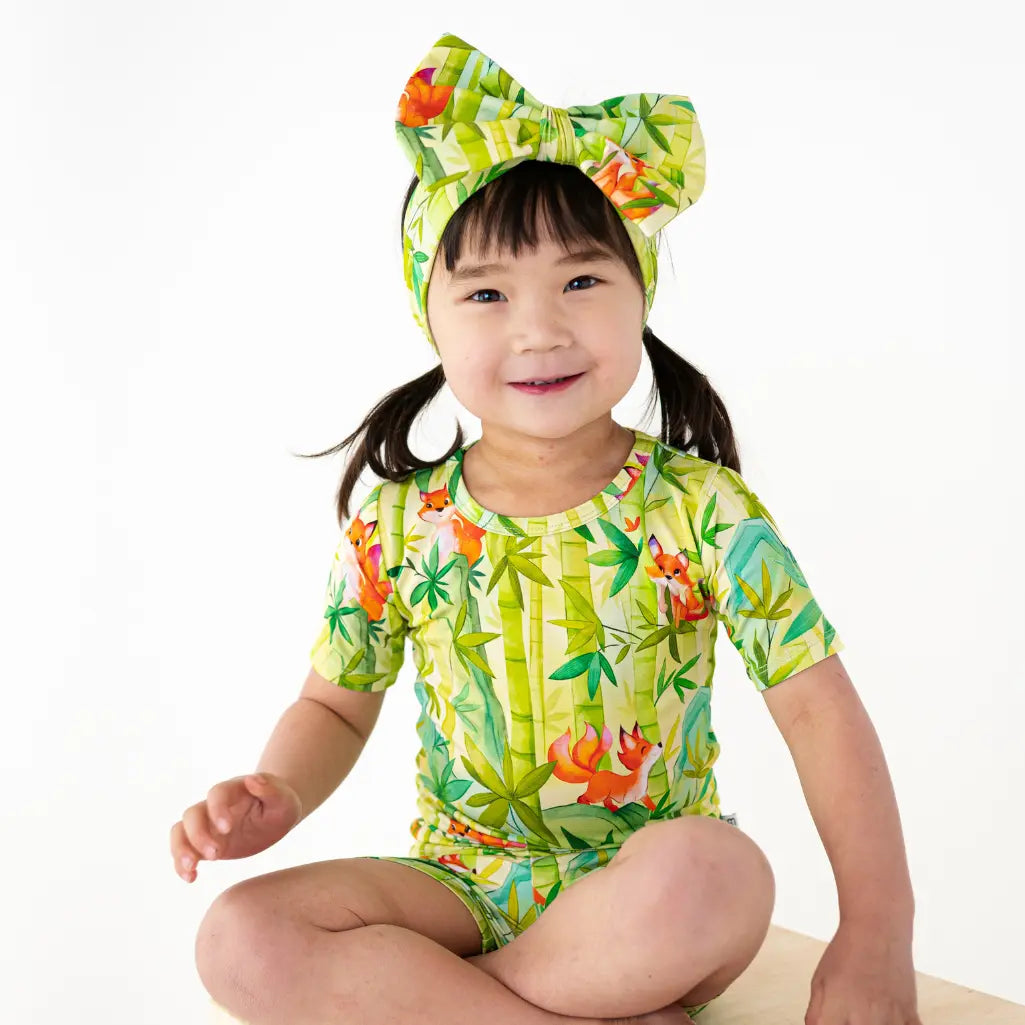 Child wearing a colorful tropical-themed swimsuit and headband on a white background
