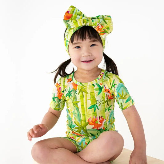 Child wearing a colorful tropical-themed swimsuit and headband on a white background