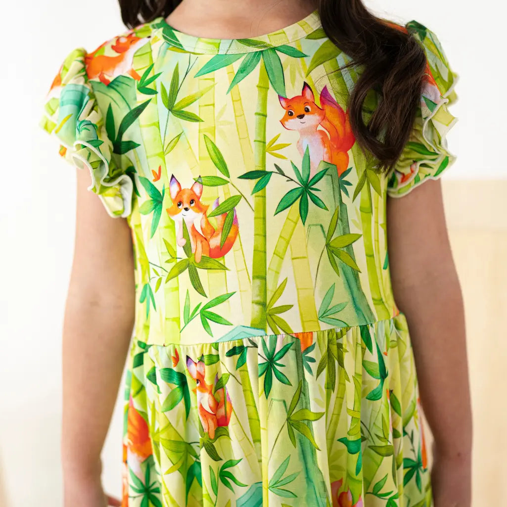 Child wearing a green dress with fox and bamboo pattern