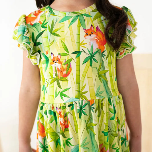 Child wearing a green dress with fox and bamboo pattern