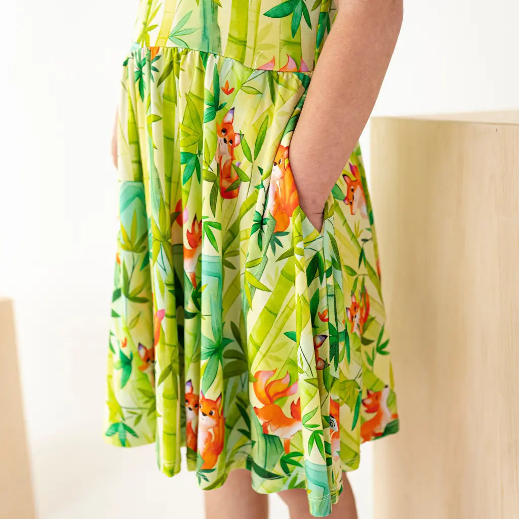 Green dress with fox and floral pattern worn by a person sitting on a beige chair.