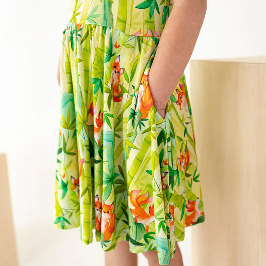 Green dress with fox and floral pattern worn by a person sitting on a beige chair.