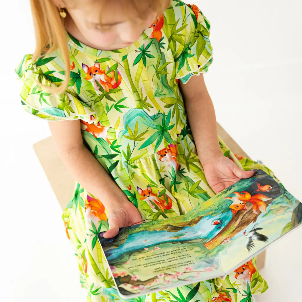 Child wearing a green dress with animal prints, holding a book with similar designs.