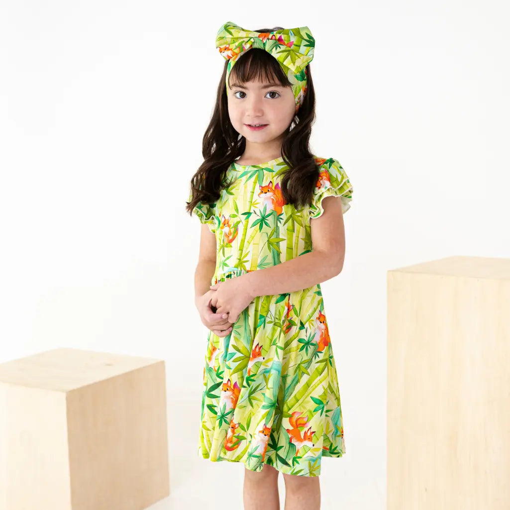Young girl wearing a green floral dress with a matching headband on a white background