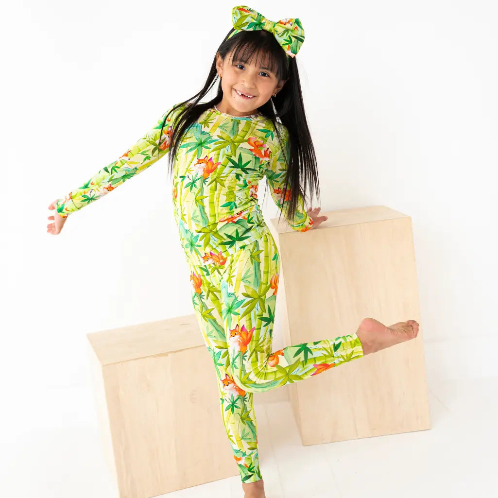 Child wearing a colorful onesie with a pattern of leaves and flowers, sitting on a wooden box.