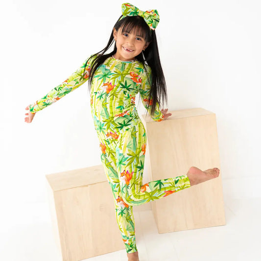Child wearing a colorful onesie with a pattern of leaves and flowers, sitting on a wooden box.