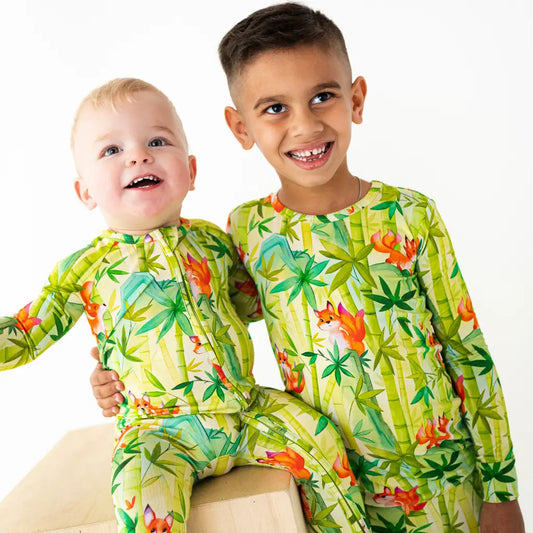 Two children wearing green pajamas with fox and tree patterns on a white background