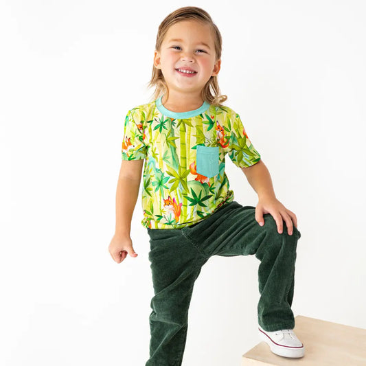 Child wearing a colorful shirt with a dinosaur pattern and green pants on a white background