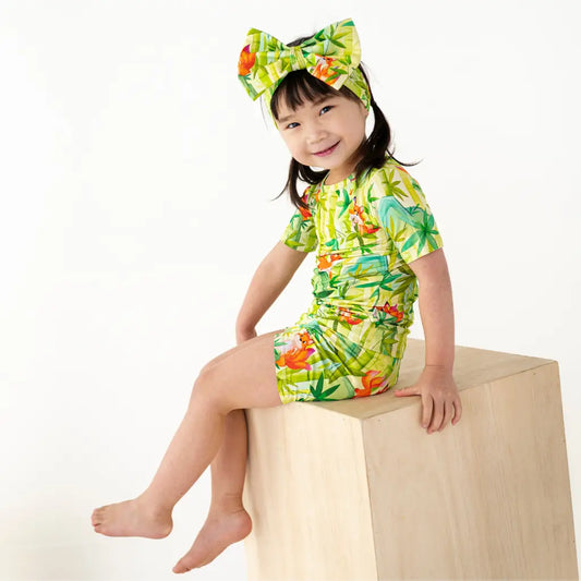 Child wearing a colorful tropical-themed outfit with a matching headband on a white background