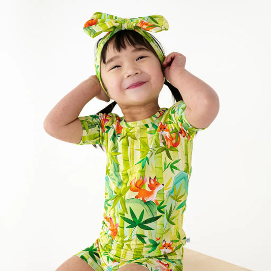 Child wearing a colorful tropical-themed outfit with a matching headband on a white background