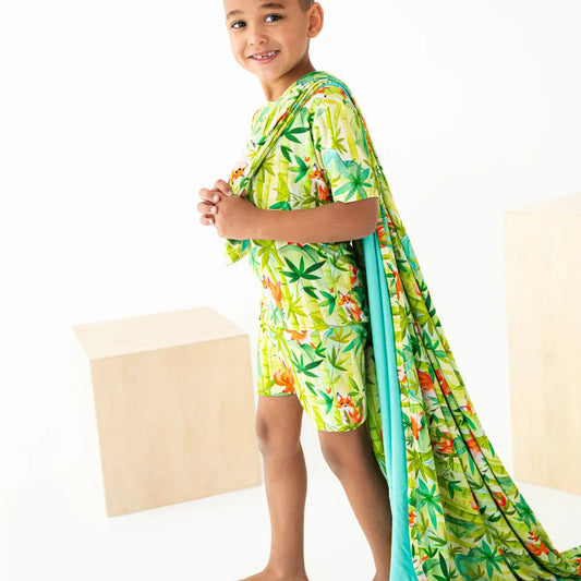 Child wearing a tropical print swimsuit with a matching towel draped over one shoulder on a white background.