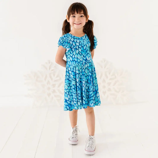 Young girl wearing a blue dress with a pattern, standing on a white background