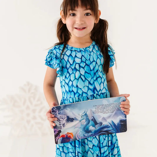 Young girl in a blue dress holding a children's book with a dragon illustration on a white background