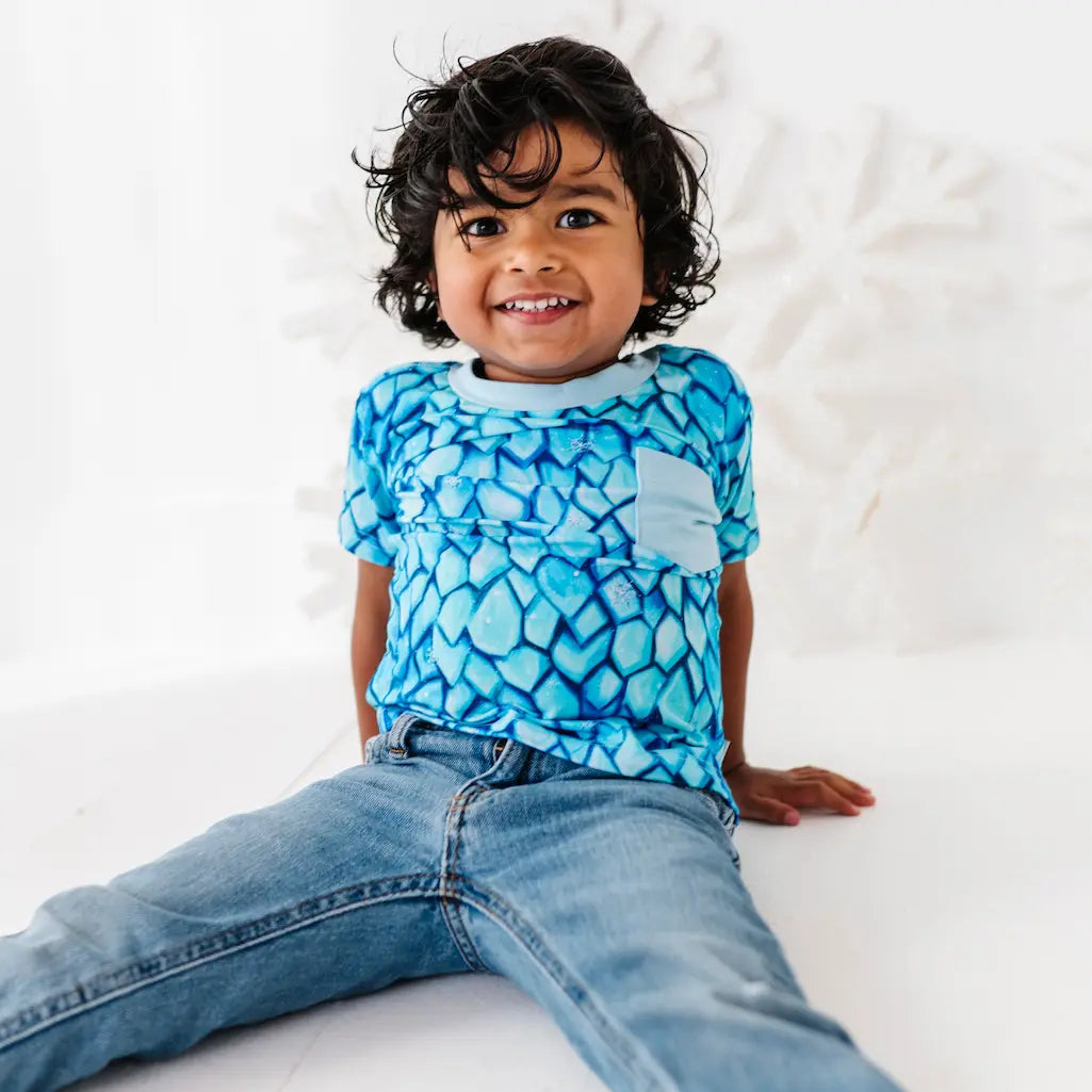 Child wearing a blue patterned shirt and jeans sitting on a white surface