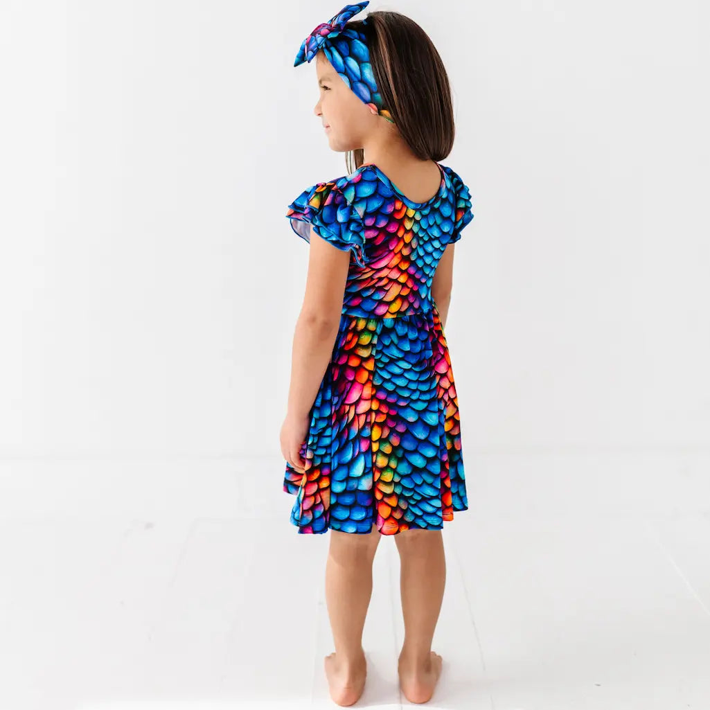 Child wearing a colorful dress with dragon scale pattern on a white background