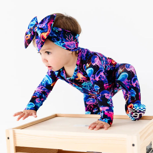 Baby in a colorful jellyfish-themed outfit and headband standing on a wooden surface.