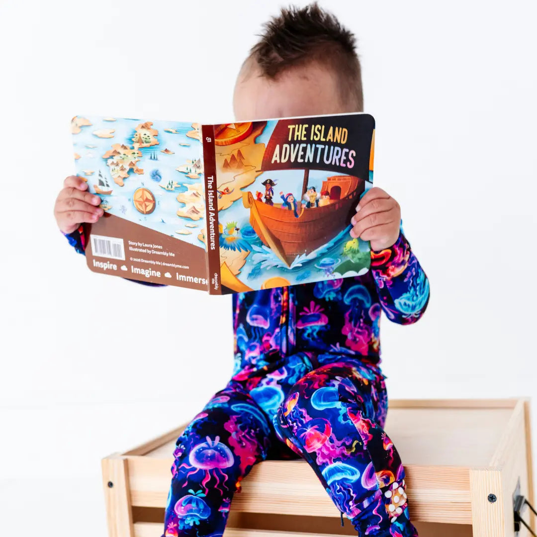 Child wearing a colorful onesie holding two books with a white background