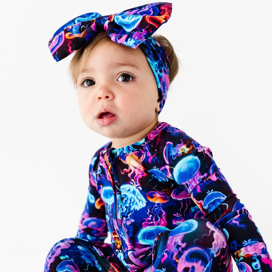 Baby wearing a colorful onesie with sea creature patterns and a matching headband.