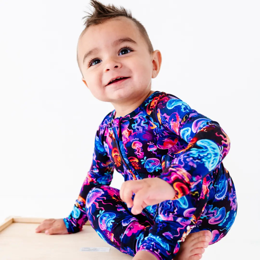 Child wearing a colorful onesie with a pattern, sitting on a white background