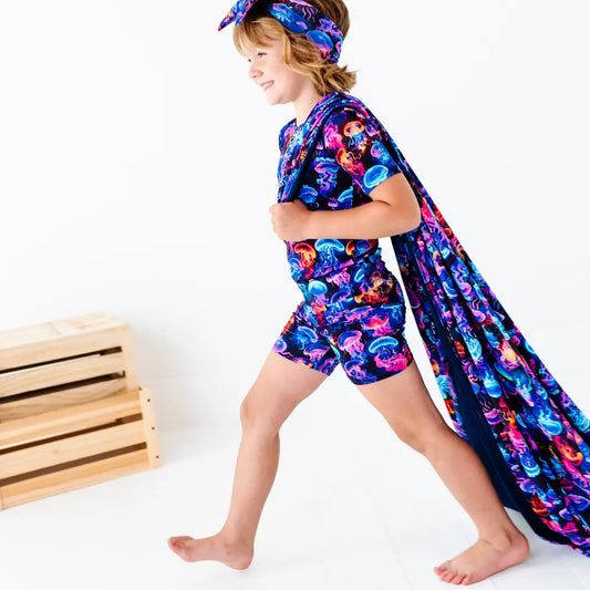 Child wearing a colorful jellyfish-themed outfit with a cape on a white background