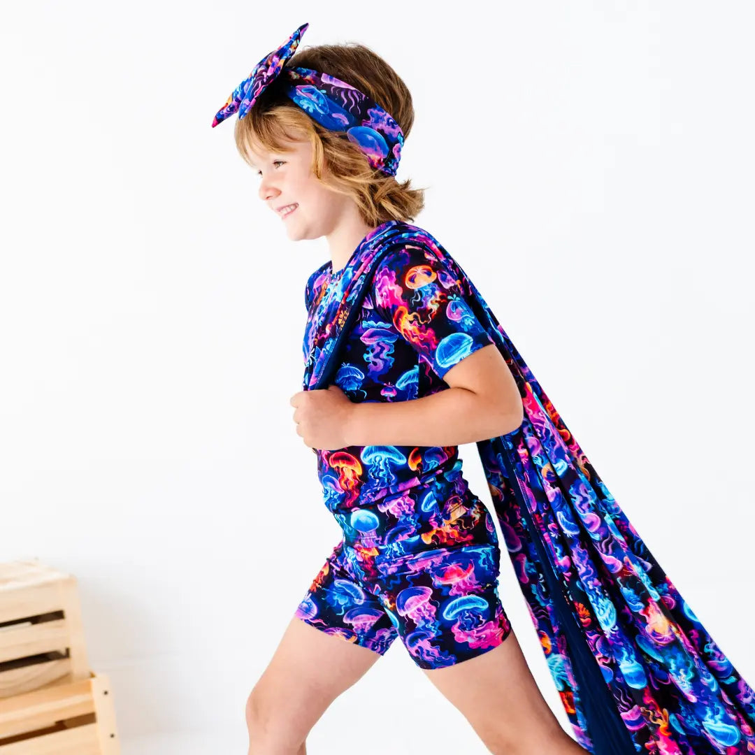 Child wearing a colorful jellyfish-themed romper and cape on a white background