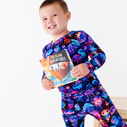 Child wearing a colorful onesie with jellyfish pattern, holding a book titled 'The Island Adventures'.