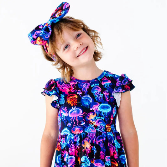 Child wearing a colorful dress with jellyfish pattern and a matching headband on a white background