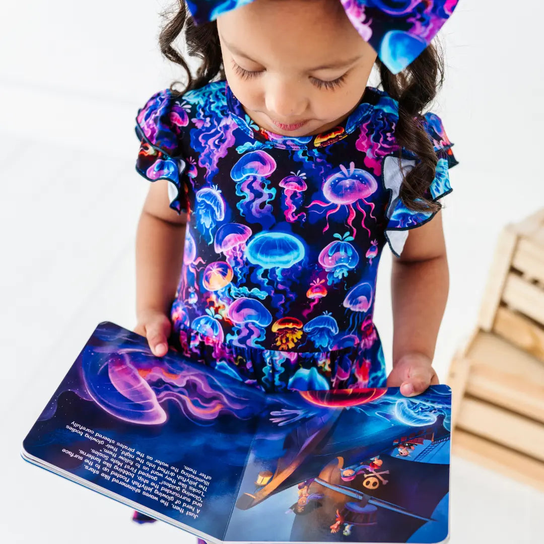 Child wearing a colorful shirt with jellyfish pattern, holding a book with similar design.