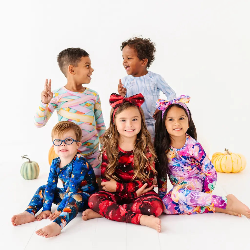 Five children wearing colorful pajamas on a white background with pumpkins.