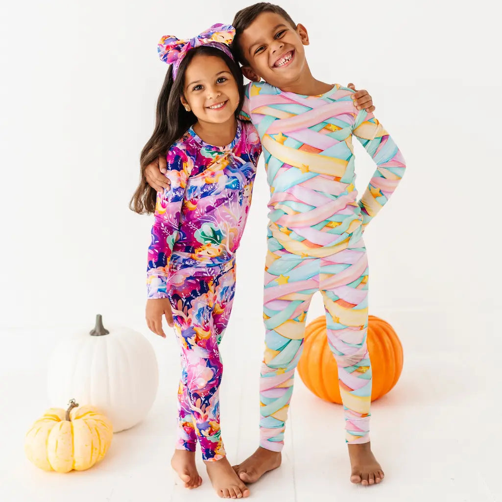 Two children wearing colorful pajamas with pumpkins in the background