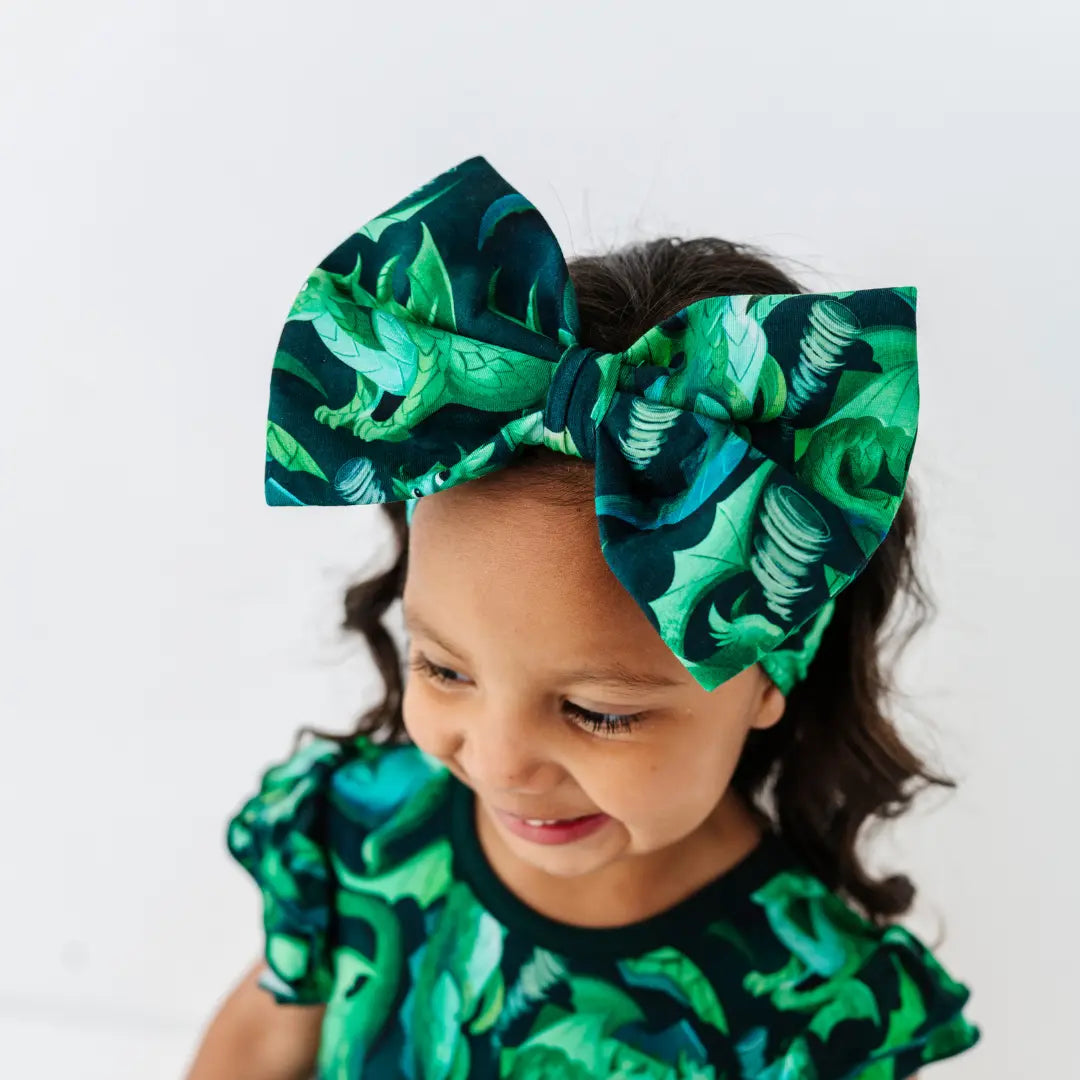 Child wearing a green dinosaur print headband and outfit on a white background