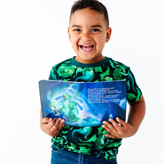 Child wearing a green dragon-patterned shirt holding a book with a dragon illustration on a white background