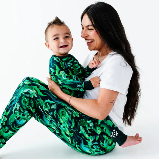 Woman and child wearing green patterned outfits sitting together on a white background