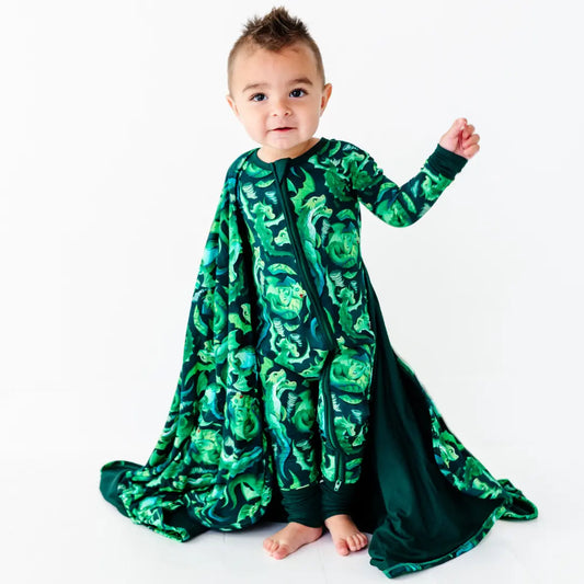 Baby wearing a green patterned onesie with a cape on a white background