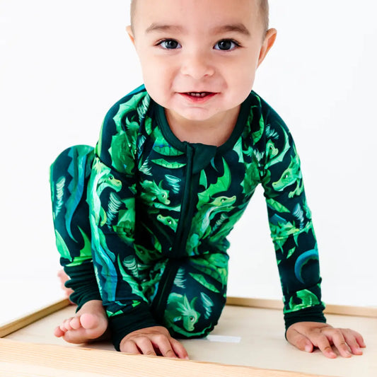 Baby wearing a green dinosaur patterned onesie on a white background