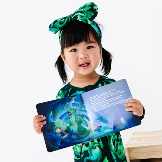 Child in a green costume holding a colorful book with a dragon illustration on a white background