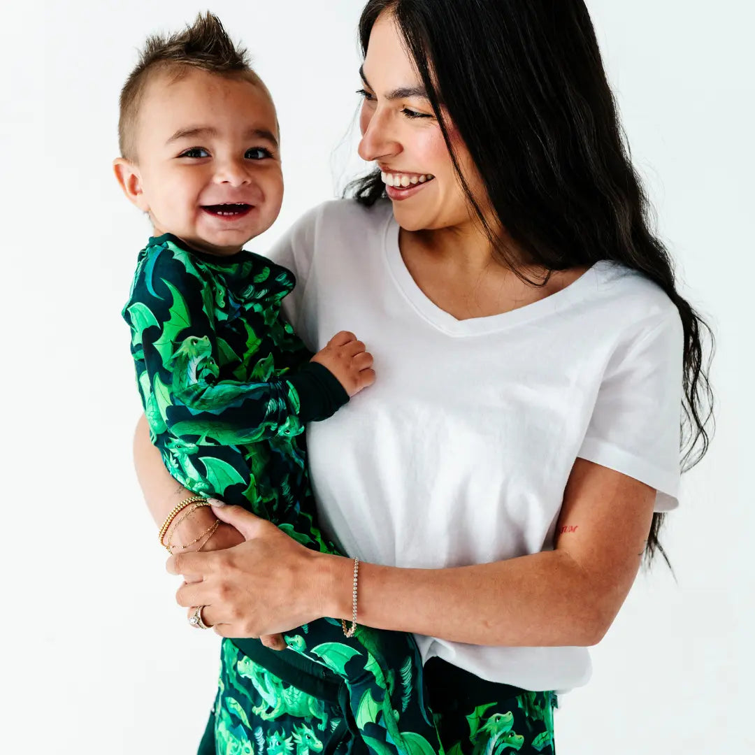 Woman holding a child wearing a green patterned outfit against a white background