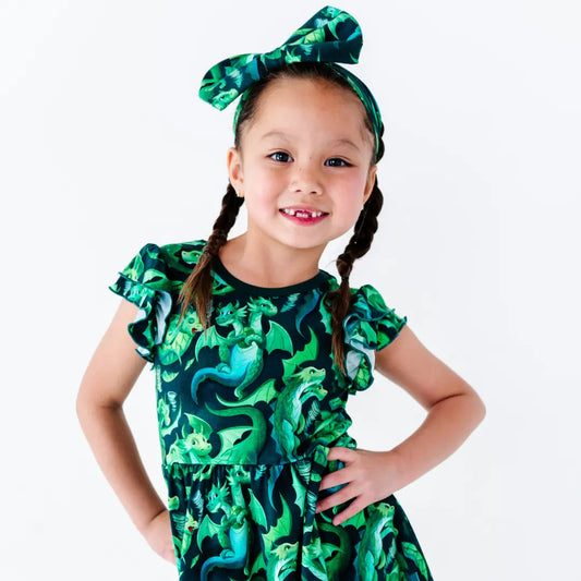 Young girl wearing a green dinosaur print dress with a matching headband on a white background