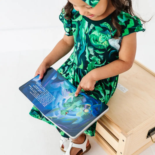 Child in a green dress with a fish pattern reading a book on a white background