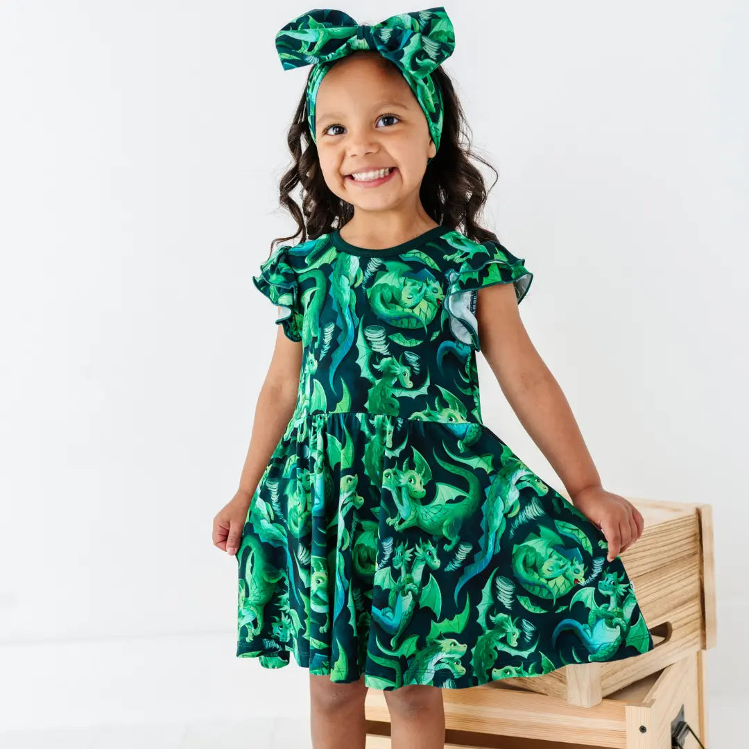 Young girl wearing a green patterned dress and headband on a white background