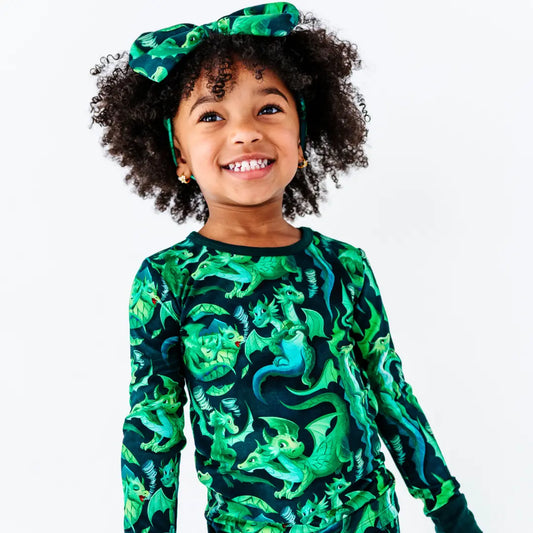 Child wearing a green dinosaur-patterned shirt with a matching headband on a white background